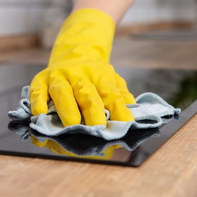 Young woman hands cleaning a modern black induction hob by a rag, housework